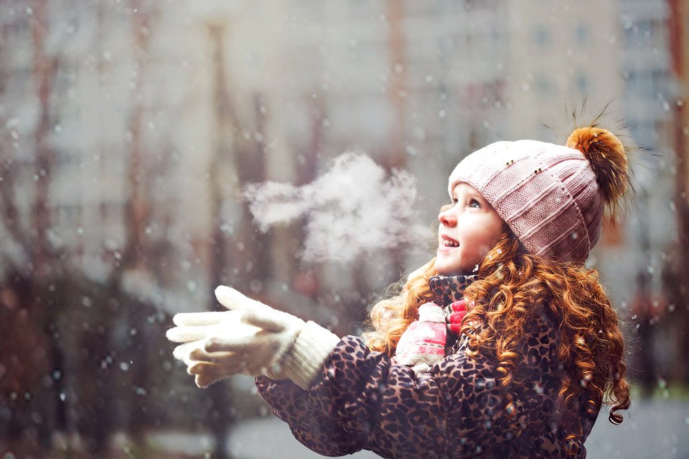 Cute little girl stretches her hand to catch falling snowflakes. First snow. Toning instagram filter.