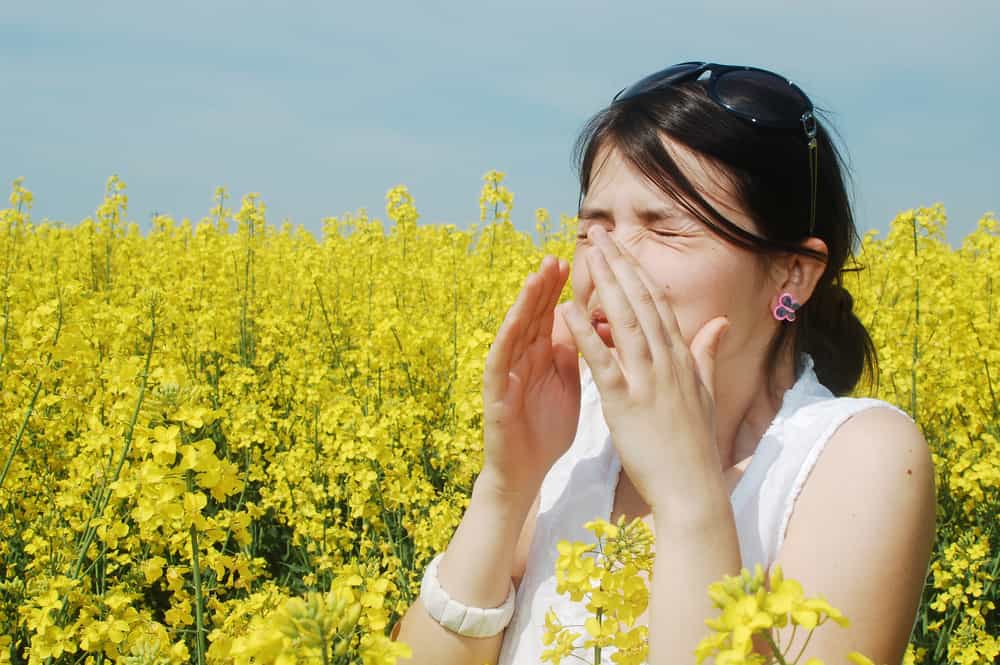 Pollen allergy, girl sneezing in a field of flowers sick