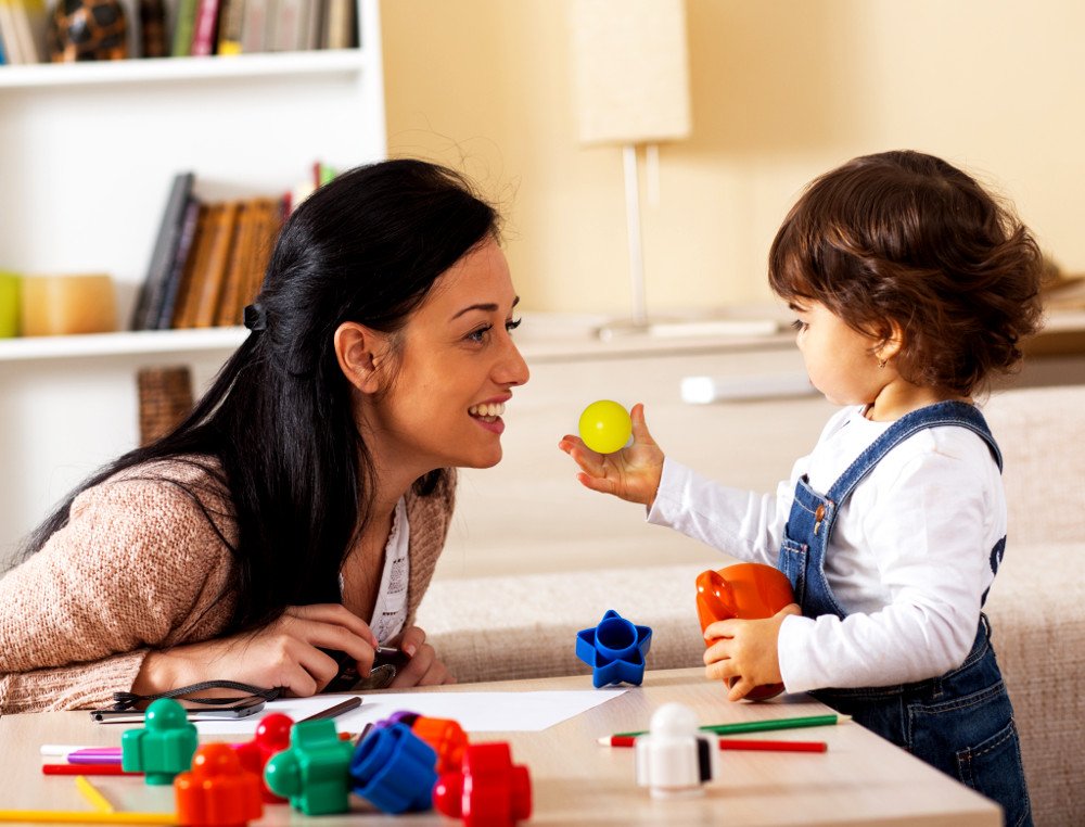 Kid handing object to mother Mother and baby girl playing with toys in living room.( Solis Images)