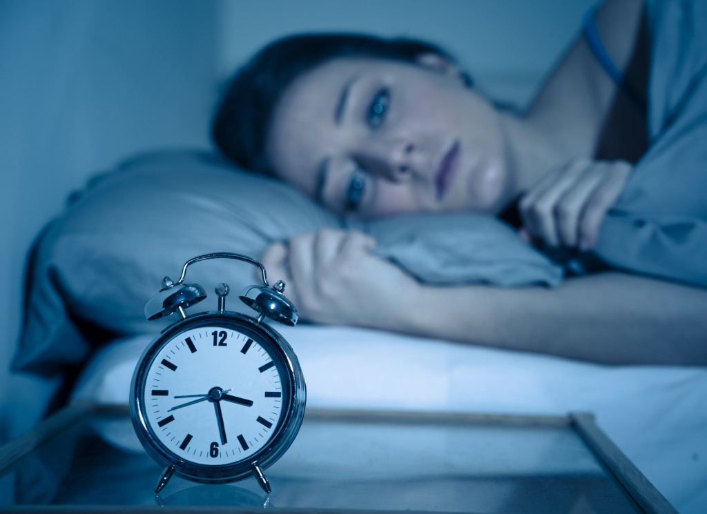 Sleepless and desperate beautiful caucasian woman awake at night not able to sleep, feeling frustrated and worried looking at clock suffering from insomnia in sleep disorder concept. - Image