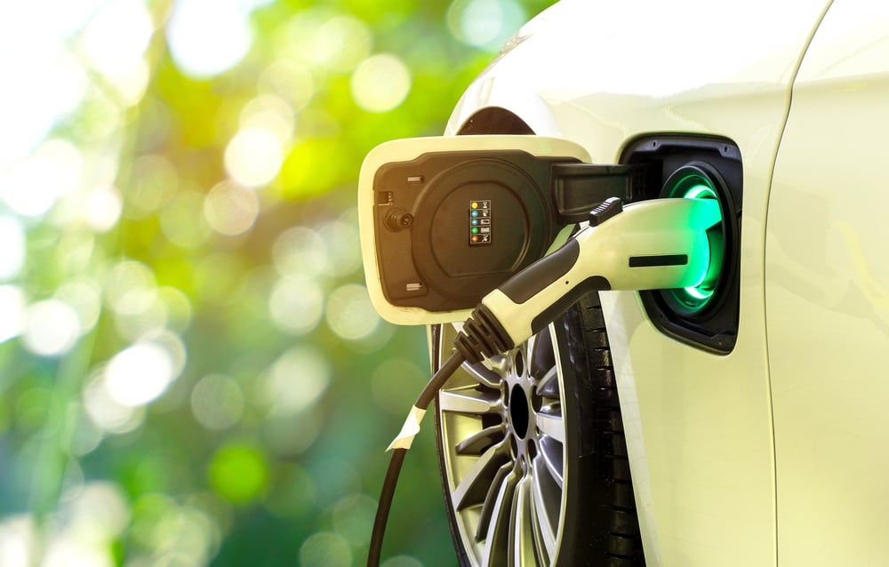 Carro EV ou carro elétrico na estação de carregamento com a fonte de alimentação conectada na natureza borrada com fundo de luz suave.  Conceito de energia alternativa ecológica - Imagem (Smile Fight) s