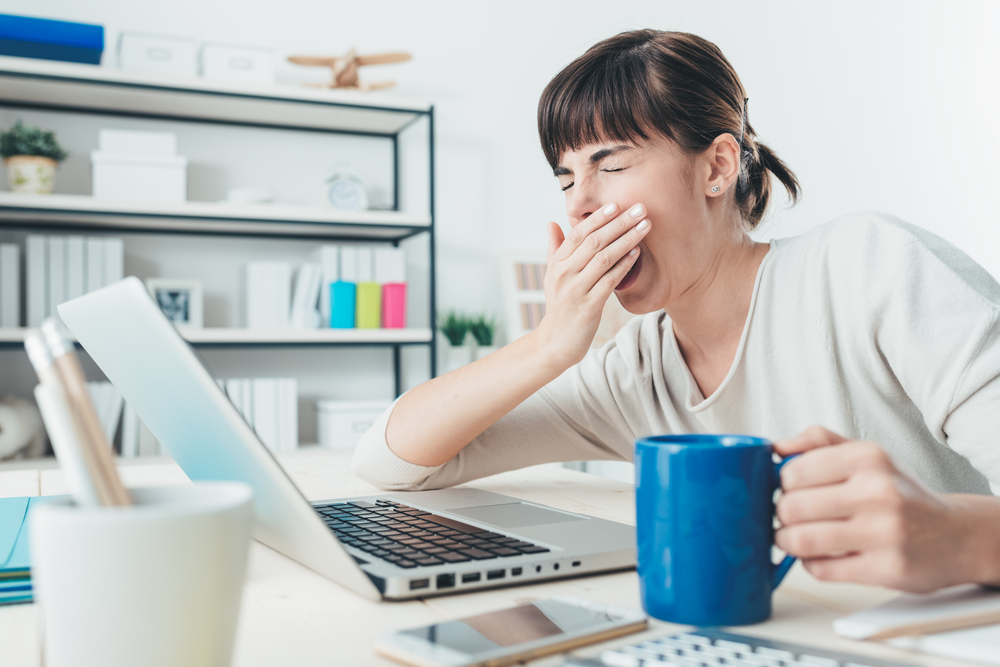 Tired sleepy woman yawning, working at office desk and holding a cup of coffee, overwork and sleep deprivation concept - Image(Stokkete)S