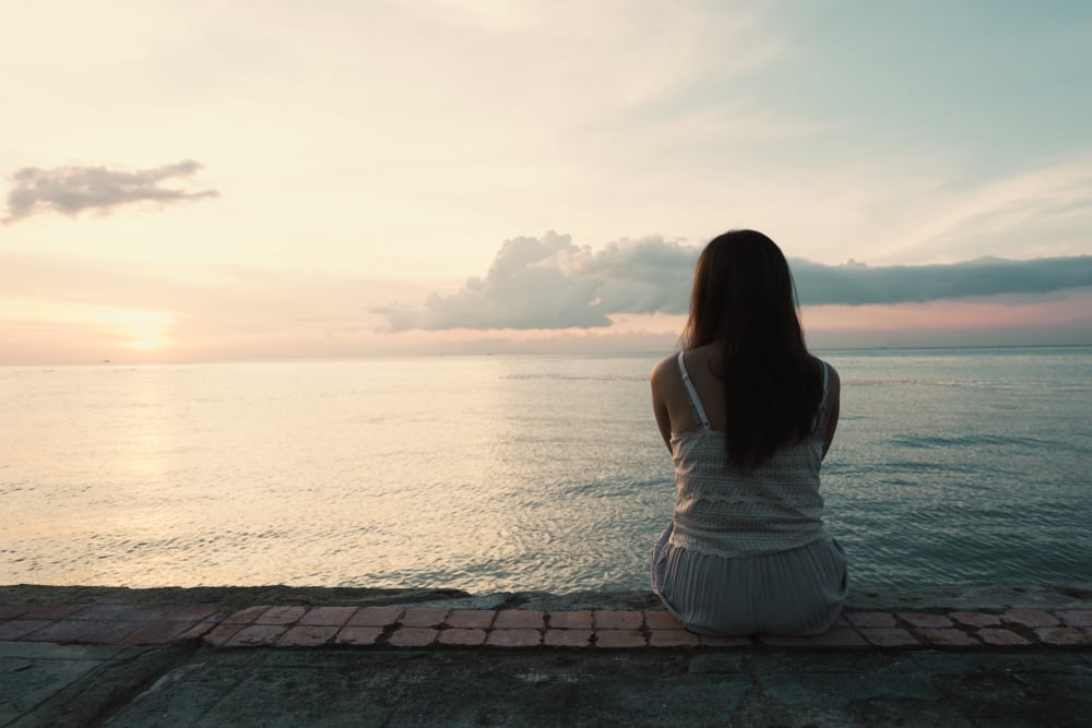 Silhouette of young woman sitting alone on back side outdoor at tropical island beach missing boyfriend and family in summer sunset. Sad and lonely concept in dark and vintage tone. - Image( AePatt Journey)