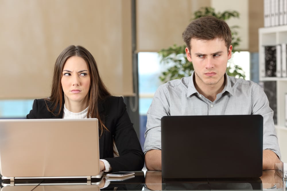 Front view of two angry businesspeople using computers disputing at workplace and looking sideways each other with envy - Image( Antonio Guillem)s