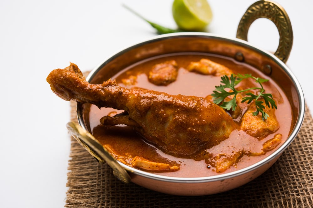 Spicy Reddish Chicken Curry Masala, with prominent Leg Piece, served in a bowl or Kadhai over colourful or wooden background( StockImageFactory.com)s