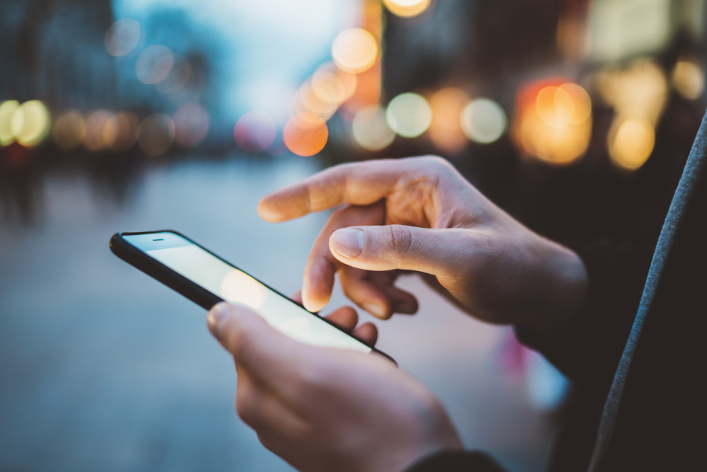 Close-up image of male hands using smartphone at night on city shopping street, searching or social networks concept(ImYanis)S