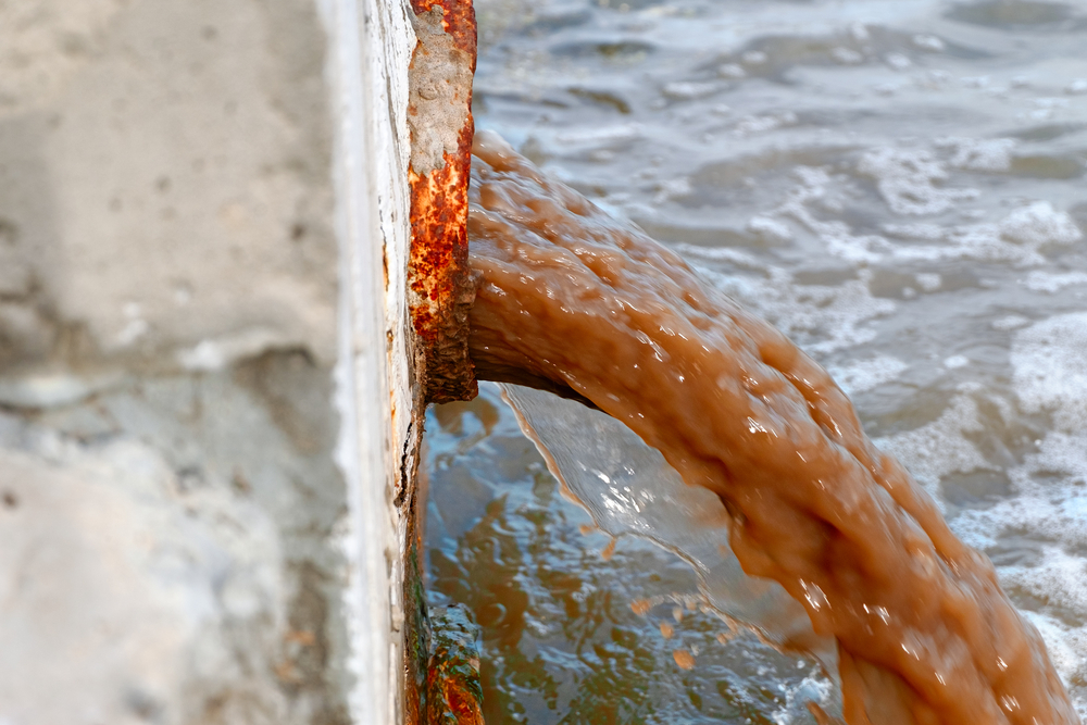 Vista lateral da água suja descarregada do cano enferrujado no rio (Mettus) S
