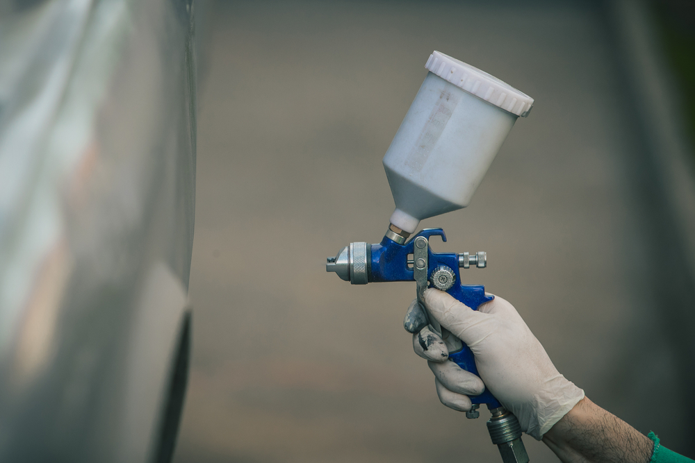 Caucasian man is spraying color with a compressed air paint gun on the vintage car as a restoration project(Anze Furlan)s