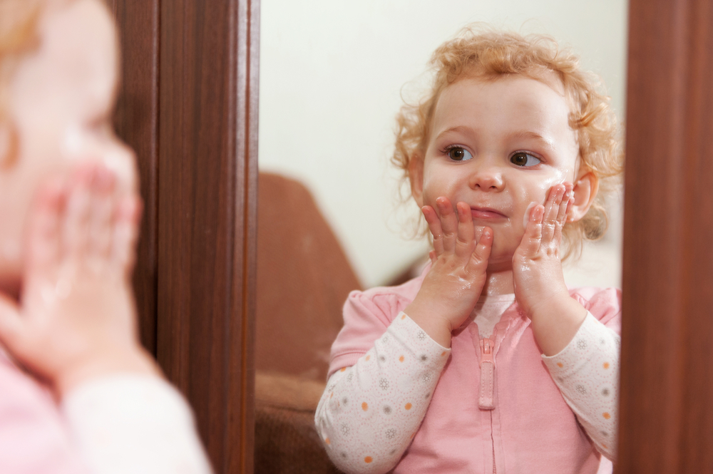 Cute baby applying cream on her cheeks looking at mirror(spass)S