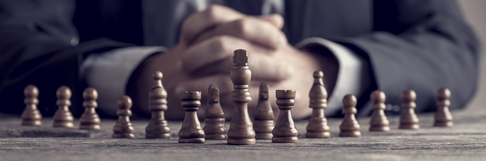 Retro style image of a businessman with clasped hands planning strategy with chess figures on an old wooden table(Gajus)S