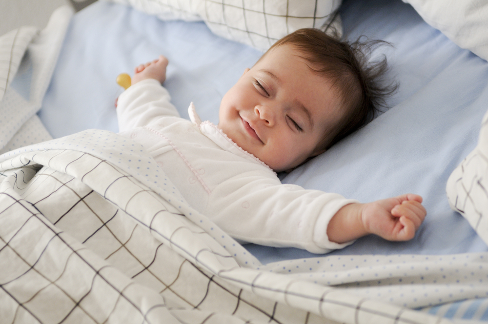 Menina sorridente deitada em uma cama dormindo em lençóis azuis (javi_indy) S