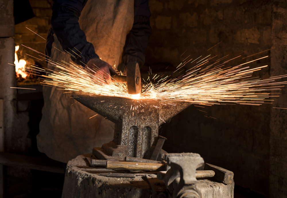 The blacksmith manually forging the molten metal on the anvil in smithy with spark fireworks(Drpixel)s