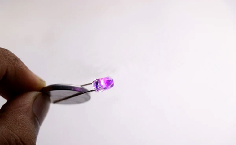 Lâmpada LED conectada à bateria de moedas que brilha na cor roxa