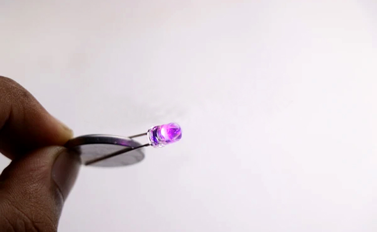 LED bulb connected to coin battery which is glowing purple in color