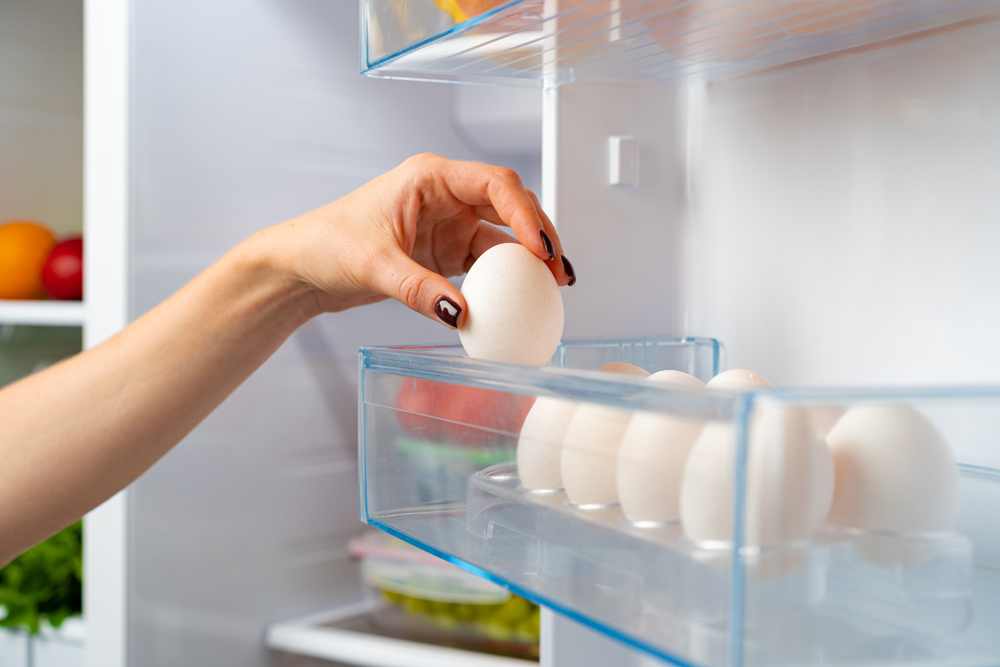 Mão feminina tirando ovo de uma geladeira de perto