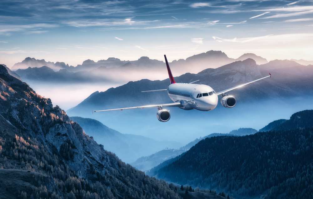 Airplane,Is,Flying,Over,Mountains,In,Fog,At,Sunset,In