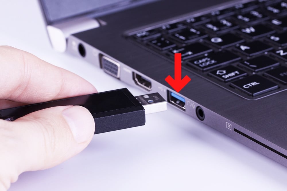 Black removable flash disk memory in fingers with laptop USB slot on white background